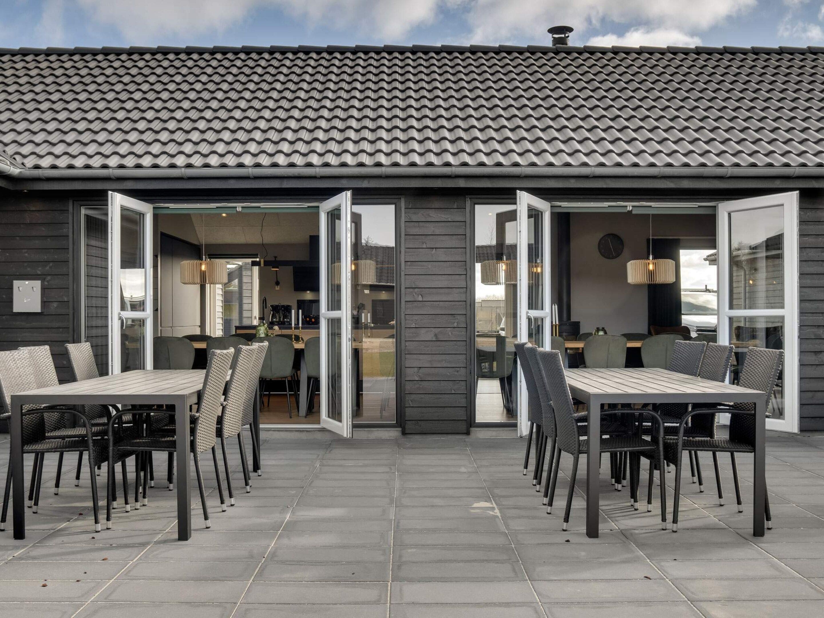 Ein modernes Gebäude mit einem Ziegeldach, einer offenen Patio mit Tischen und Stühlen sowie einer sichtbaren Küchenzeile.