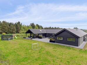 A modern building with a covered patio area, a fenced play area, and a soccer goal. - 5 Star Holiday Home in Norre Nebel (Norre Nebel)