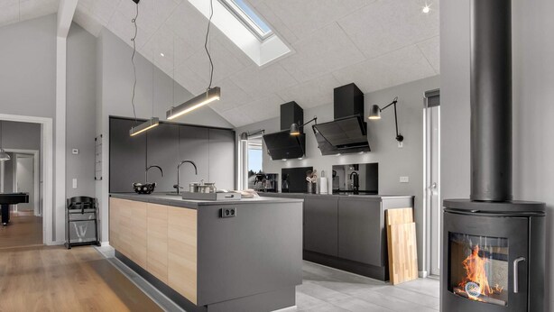 A modern kitchen with a central island, built-in appliances, and a wood-burning stove. - 5 Star Holiday Home in Norre Nebel (Norre Nebel)