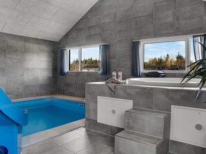 A modern bathroom with a built-in bathtub, grey tiled walls, and windows with curtains. - 5 Star Holiday Home in Norre Nebel (Norre Nebel)
