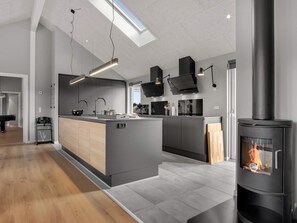 A modern kitchen with a central island, built-in appliances, and a wood-burning stove. - 5 Star Holiday Home in Norre Nebel (Norre Nebel)