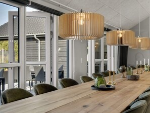 A dining area with a long wooden table, multiple chairs, and hanging pendant lights. - 5 Star Holiday Home in Norre Nebel (Norre Nebel)