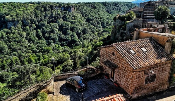 A stone building with a tiled roof, surrounded by lush greenery and a steep cliff.