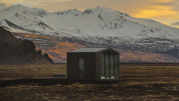 A small, isolated cabin with a glass door, situated in a barren landscape with a snow-capped mountain in the background.