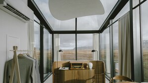 A modern room with a large window, a wooden table, a sofa, and a hanging coat rack.