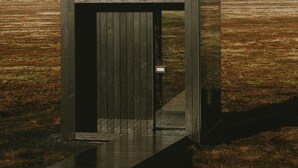 A wooden structure with a door, a pathway leading to it, and a rainbow in the background.