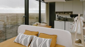 Een moderne slaapkamer met een groot bed, uitzicht op zee en een minimalistische keukenhoek.