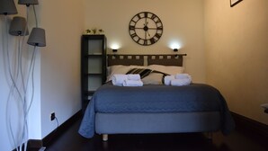 A bedroom with a bed, a wall clock, a shelf with plants, and lamps.