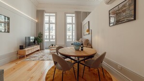 A modern living room with a wooden dining table, four chairs, a TV, and a large window with curtains. - Heart OF Porto Apartment A by Vacationy (Porto)
