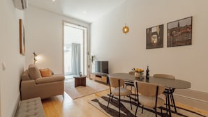 A modern living room with a sofa, dining table, and chairs, a TV, and artwork on the wall.