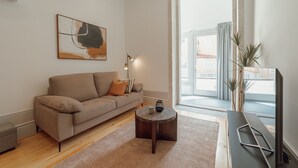 A modern living room with a sofa, a coffee table, a painting, and a view through a large window.