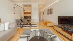 A modern living room with a sofa, a glass coffee table, a TV, and a dining area with chairs and a table.