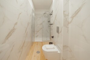 A modern bathroom with a glass-enclosed shower, a toilet, and a sink.