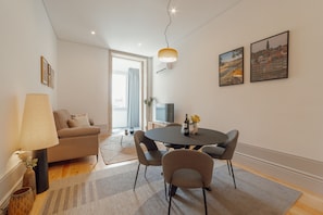 A modern living room with a sofa, a round dining table with chairs, a lamp, and two framed pictures on the wall.