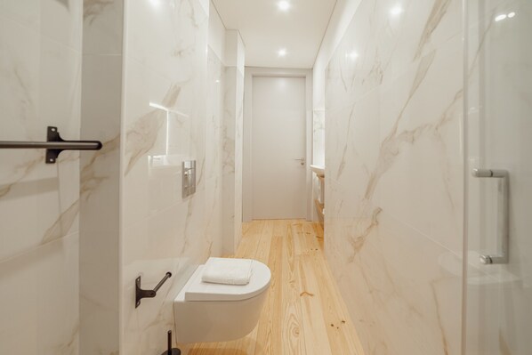 Un baño moderno con suelo de madera, paredes de mármol blanco y un inodoro blanco.