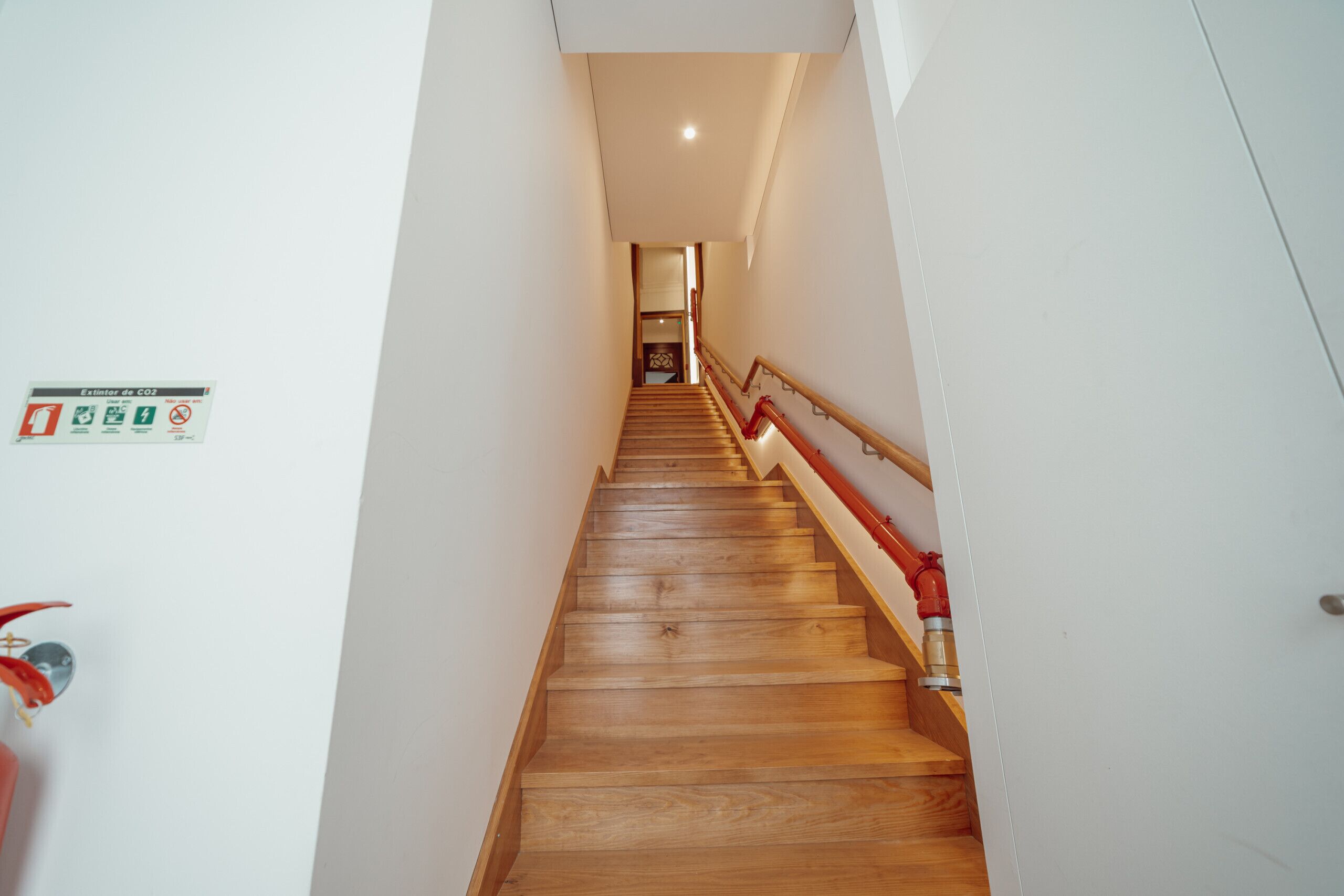 Eine Holztreppe mit roter Handlauf, weißen Wänden und einem CO2-Monitor-Schild.