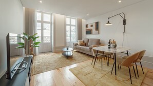 A modern living room with a sofa, dining table, and chairs, a TV, and a plant.