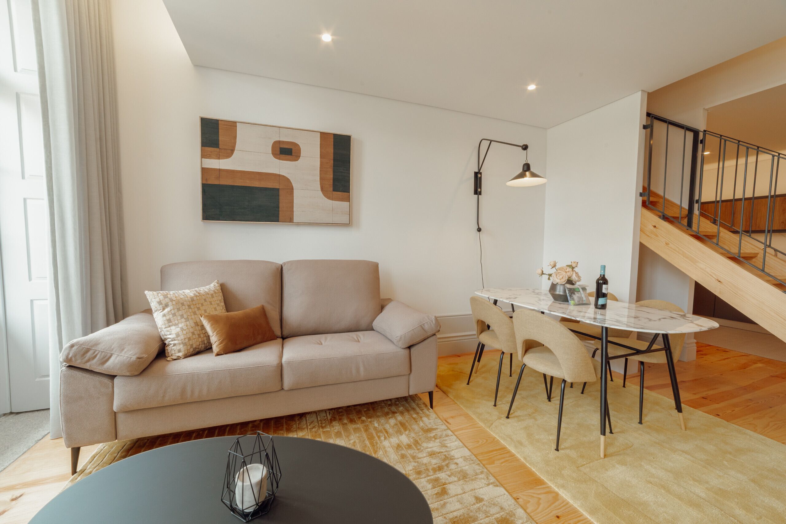 A modern living room with a sofa, a dining table, and a staircase.