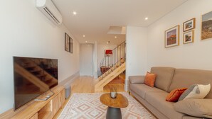 A modern living room with a large flat-screen TV, a wooden coffee table, a beige sofa, and a patterned rug. - Heart OF Porto Apartment F Duplex by Vacationy (Porto)