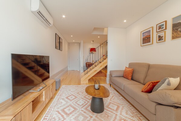A modern living room with a large flat-screen TV, a wooden coffee table, a beige sofa, and a patterned rug.