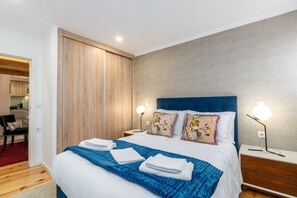A hotel room with a bed, two bedside lamps, a nightstand, a wooden wardrobe, and a view of the adjacent room. - City Center Comfort Apartment B by Vacationy (Porto)