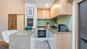 A modern kitchen with a built-in oven, a microwave, and a coffee machine. There is a white chair and a green bowl on the counter. - City Center Comfort Apartment B by Vacationy (Porto)