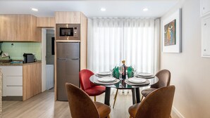A modern kitchen with a built-in microwave and refrigerator, a dining area with a round table set for four, and a large window with sheer curtains. - City Center Comfort Apartment B by Vacationy (Porto)