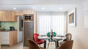A modern kitchen with a built-in microwave and refrigerator, a dining area with a round table set for four, and a large window with sheer curtains.