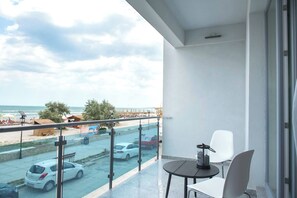 Un balcon avec vue sur la plage et la circulation, une table avec des chaises et une porte vitrée.