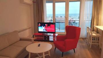 A living room with a sofa, a red armchair, a small round table, and a TV displaying a sports event.