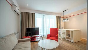 A modern living room with a sofa, a red armchair, a white coffee table, a TV, and a desk with shelves. - Wave 1 Promenada Apartments (Navodari)