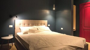 A neatly made bed with a tufted headboard, a bedside table with a lamp, and a red door in the background. - Wave 1 Promenada Apartments (Navodari)