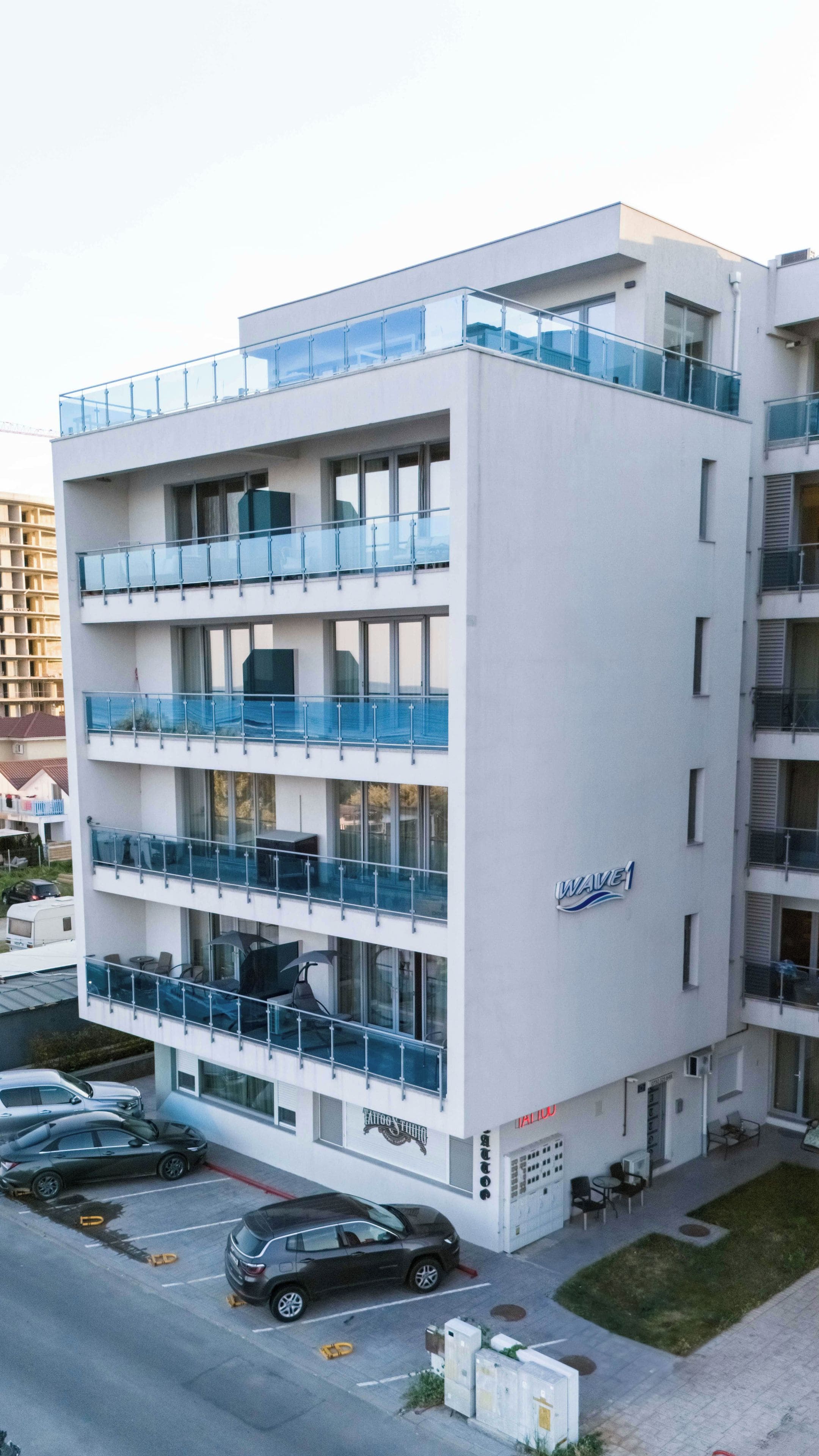 A multi-story hotel with balconies, a visible sign for a tattoo studio, and a parking area with cars.