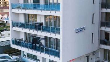 A multi-story hotel with balconies, a visible sign for a tattoo studio, and a parking area with cars.