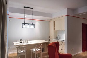 A modern kitchen with white cabinets, a white countertop, and a red chair.