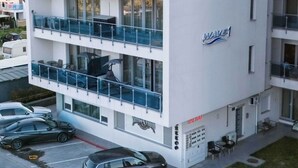 A multi-story hotel with balconies, a visible sign for a tattoo studio, and a parking area with cars. - Wave 1 Promenada Apartments (Navodari)