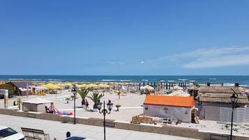 A beachside area with umbrellas, a small building, and a view of the ocean.