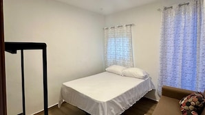A simple, clean room with a bed, a small sofa, and a window with curtains. - Residencial Fe y Esperanza (Pedernales)