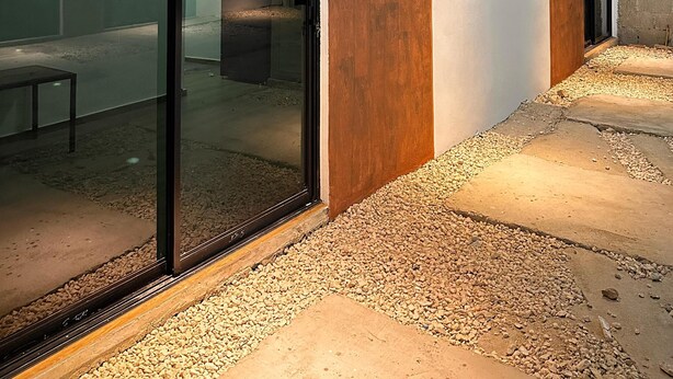 A modern building with large glass doors, a concrete pathway, and a wooden column. - Residencial Fe y Esperanza (Pedernales)