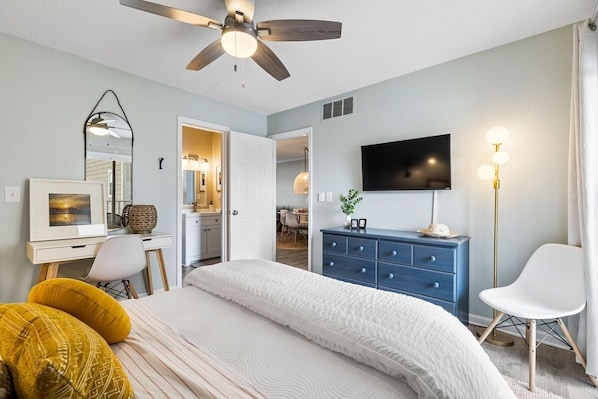 A bedroom with a bed, a desk, a dresser, a TV, and a ceiling fan.