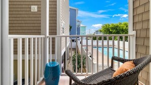 A balcony with a wicker chair and a blue vase, overlooking a swimming pool and neighboring houses. - Shell Shocked - Short, Breezy Walk to the Beach (Carolina Beach)