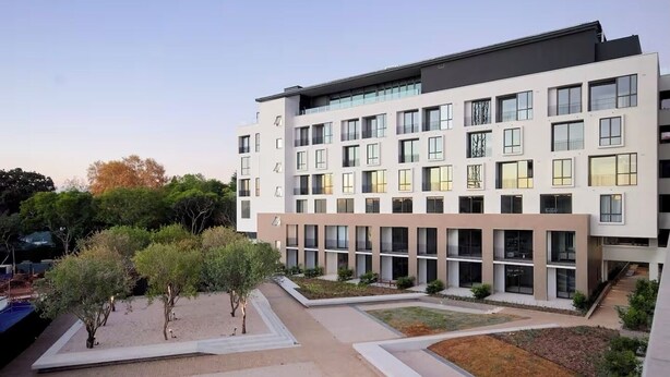 A modern multi-story building with a flat roof, large windows, and a courtyard with trees and pathways.
