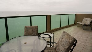 Ein Balkon mit einem Glastisch und Stühlen, Blick auf das Meer und ein gemustertes Kissen.