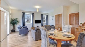A modern living room with a dining area, grey sofas, a wooden dining table set, and a potted plant. - Outlook Cottage - well look at my view! (Wandylaw)
