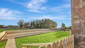A grassy outdoor area with a wooden fence, a stone wall, and a paved path. - Outlook Cottage - well look at my view! (Wandylaw)