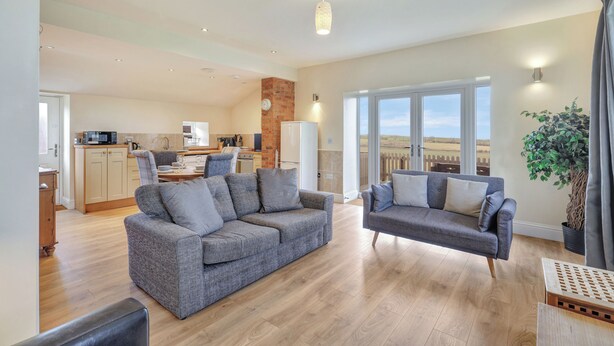 A spacious living area with a grey sofa set, a dining table, and a kitchen in the background. - Outlook Cottage - well look at my view! (Wandylaw)