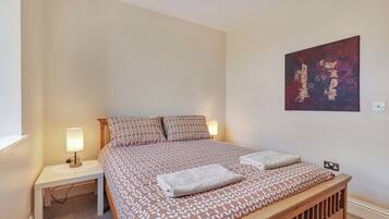 En snyggt bäddad säng med mönstrat sänglinne, två sänglampor och ett konstverk som hänger på väggen.