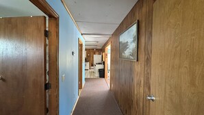 Ein schmaler Flur mit Holzwänden und -türen, der in einen Küchenbereich mit Kühlschrank und Herd führt.