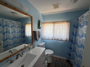 Baño con lavamanos blanco, espejo y retrete. Dos toallas cuelgan de la pared.