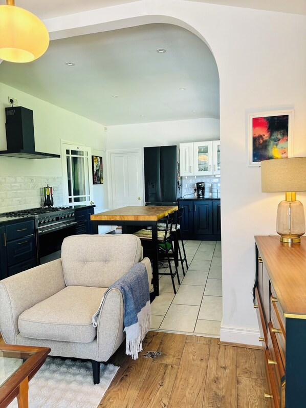 A modern kitchen with a dining area, featuring a sofa, a wooden table, and a lamp.